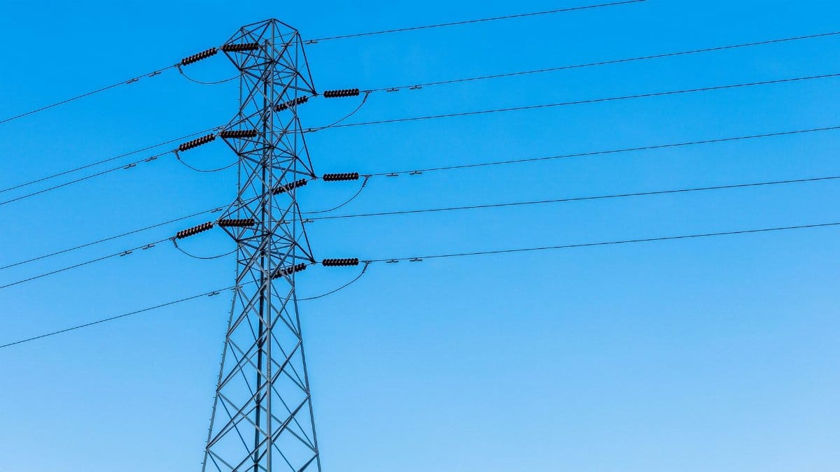A high voltage transmission tower with power lines under a bright blue sky, showcasing infrastructure.
