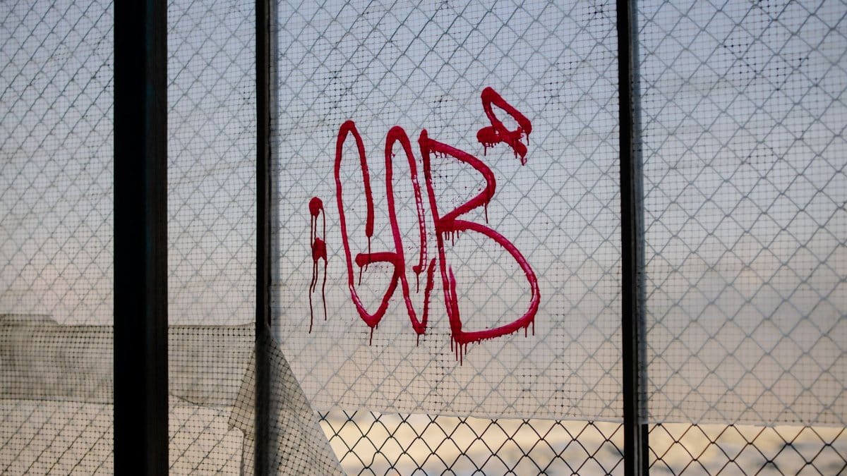 Red graffiti on a cracked window pane of an abandoned building, against a city backdrop.