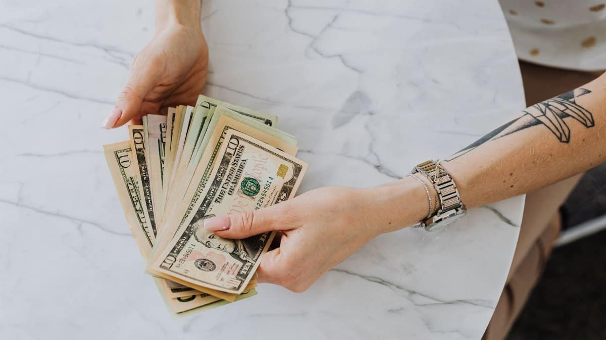 Hands holding and counting US dollar bills on a marble table, depicting wealth and finance.