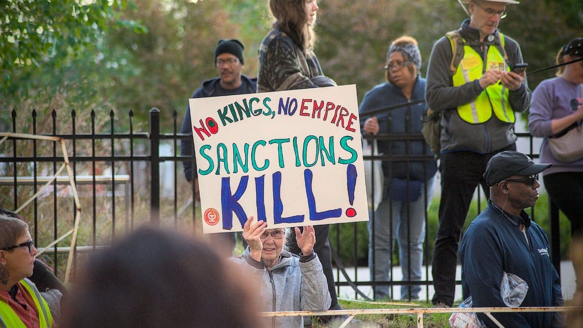Protesters gather in Towson with signs against sanctions, advocating for peace and justice.