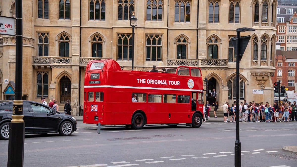 Vintage red double-decker bus offering tours in historic London with people nearby.