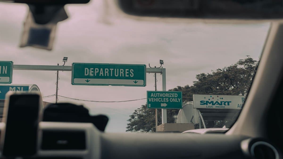 View through windshield of car driving towards airport departure signs and authorized vehicle only lane, captured in soft daylight.