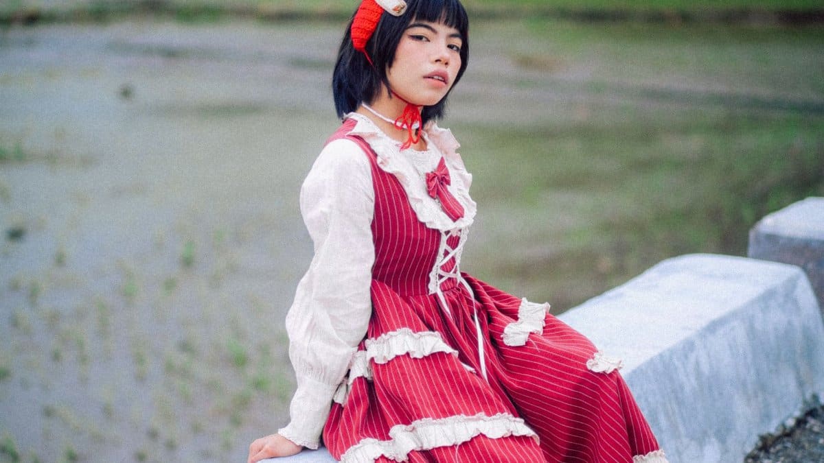 A young woman with short hair, wearing a red dress, sitting outdoors on a concrete ledge.