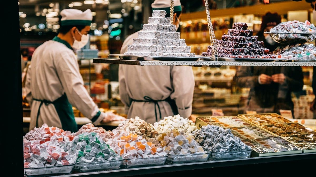 Male sellers in uniform and face mask standing at counter in confection shop near showcase with assorted delicious Turkish delight sweets