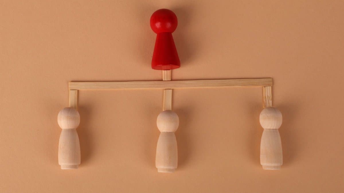 Minimalist arrangement of wooden figures depicting hierarchy and leadership concept.