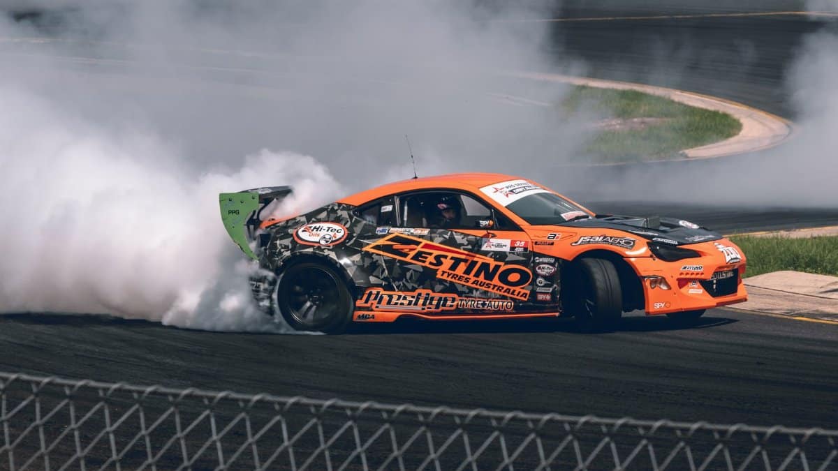 Orange drift car in action on a race track, producing smoke during a motorsport event in Australia.
