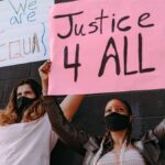Two protesters holding placards demanding equality and justice for all, wearing face masks outdoors.