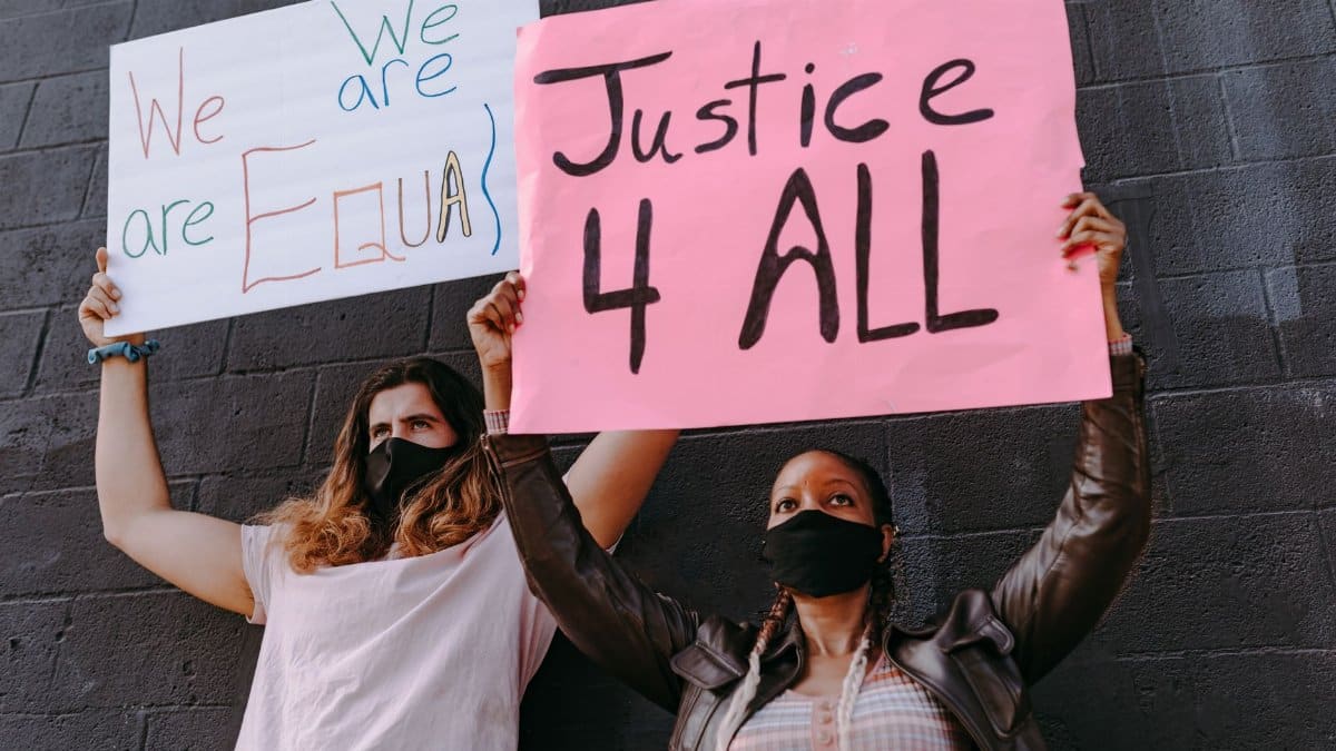 Two protesters holding placards demanding equality and justice for all, wearing face masks outdoors.