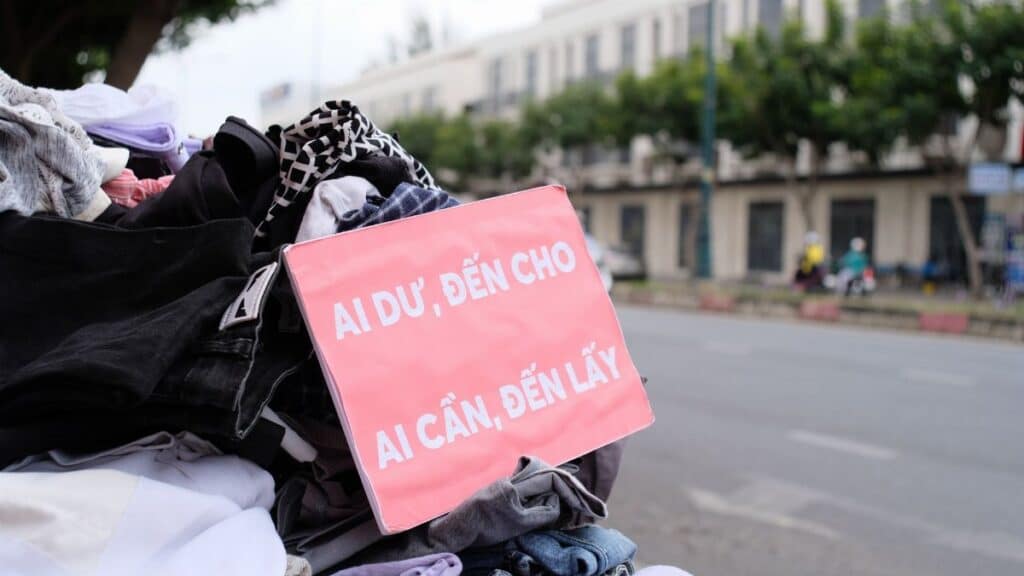 Clothes donation on city street with sign offering free items to those in need.