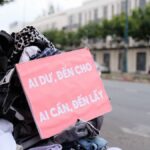 Clothes donation on city street with sign offering free items to those in need.