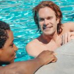 Two friends relaxing and chatting at a swimming pool during a sunny day. Enjoyment of vacation.