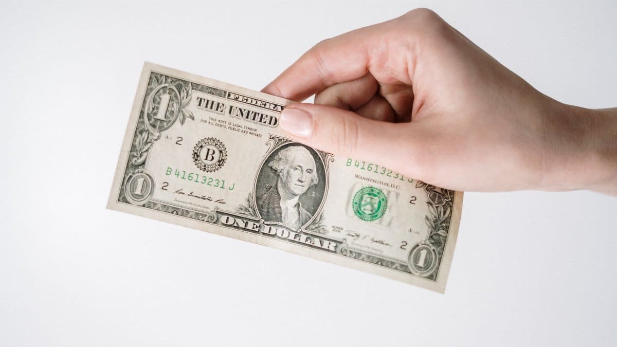 Close-up of a Caucasian hand holding a US one dollar bill against a white background.