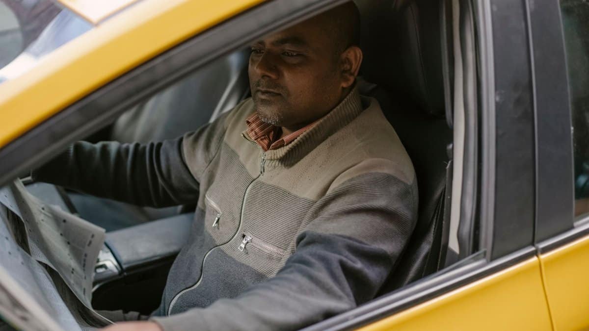 Ethnic male driver reading daily newspaper with interest while sitting in car and having break