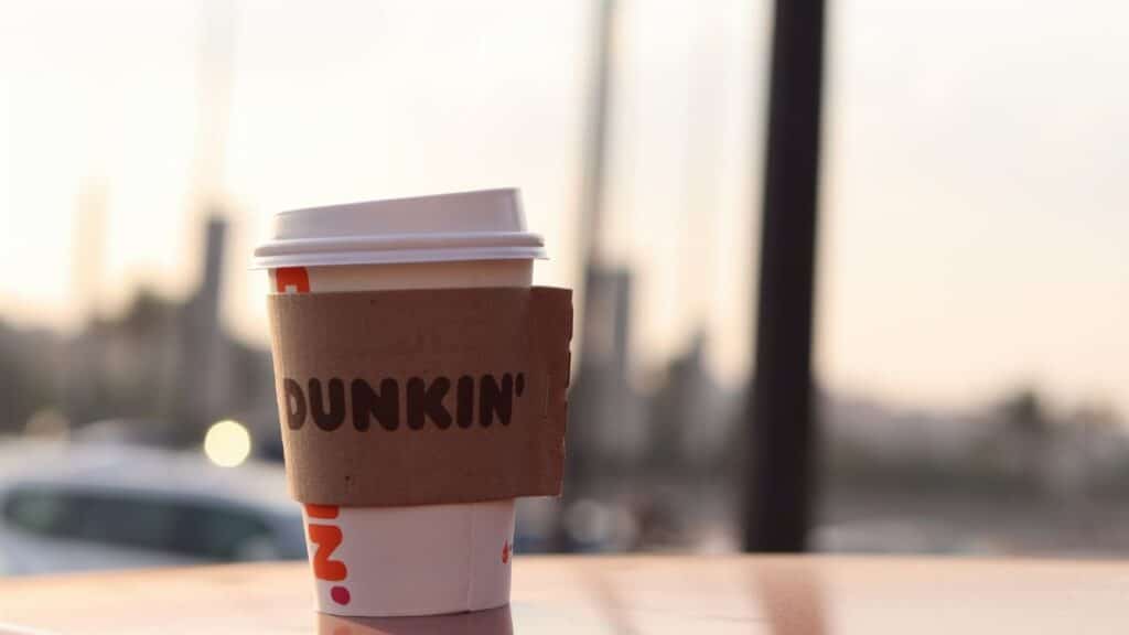 A Dunkin' coffee cup stands outdoors on a surface, captured in soft evening light.