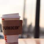 A Dunkin' coffee cup stands outdoors on a surface, captured in soft evening light.