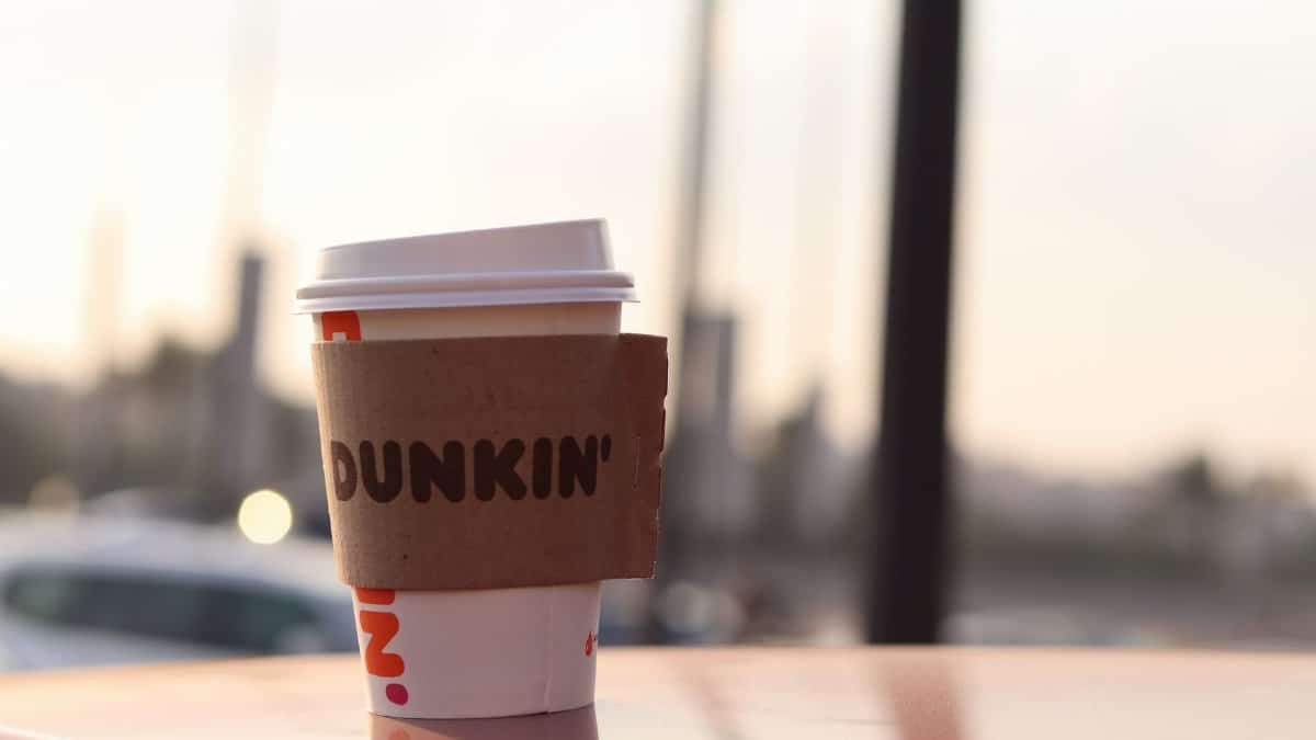 A Dunkin' coffee cup stands outdoors on a surface, captured in soft evening light.