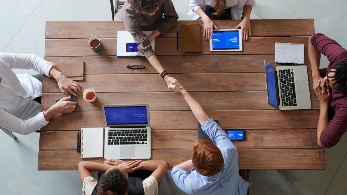 Overhead view of colleagues in a work meeting using laptops and tablets, emphasizing teamwork and technology.