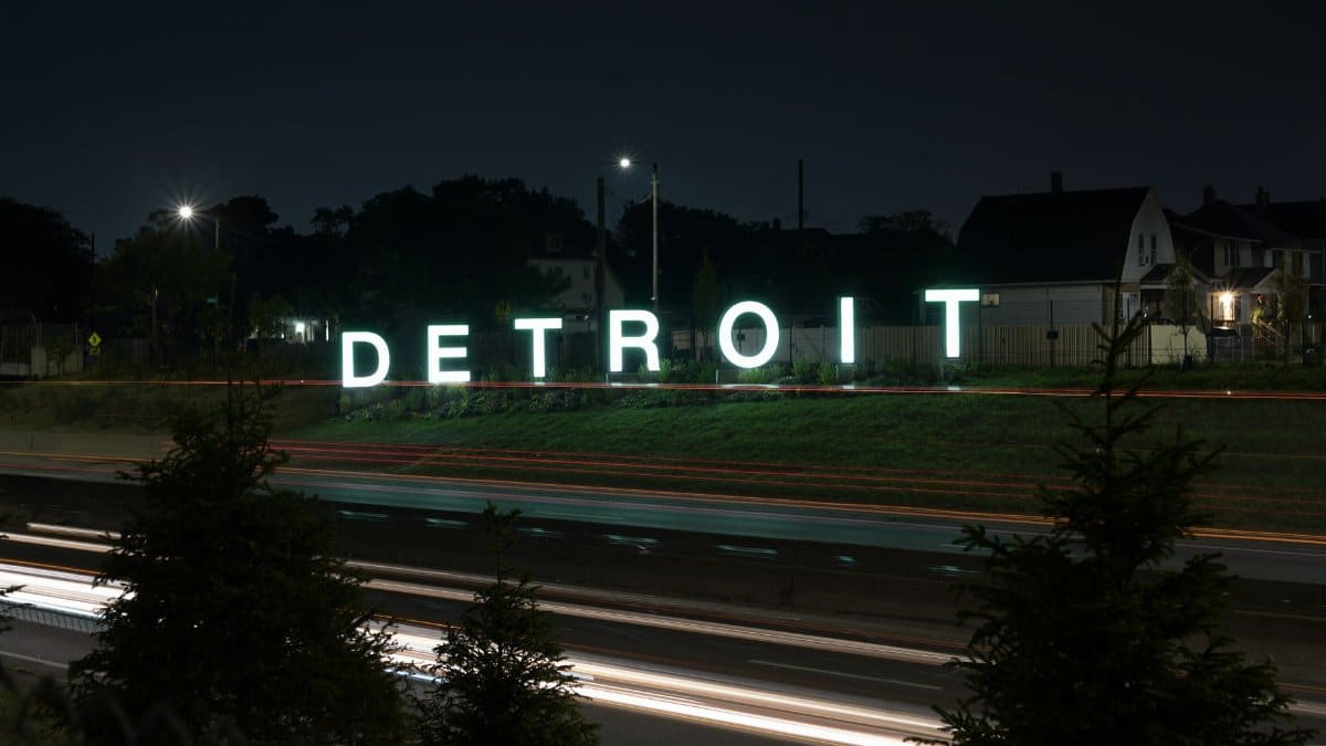 Illuminated Detroit sign at night with motion blur from passing traffic on the highway.