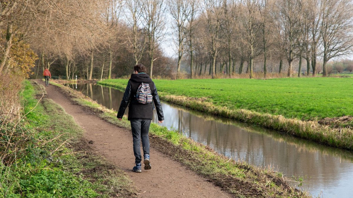Two people walking on a tranquil riverside path surrounded by nature in early spring.