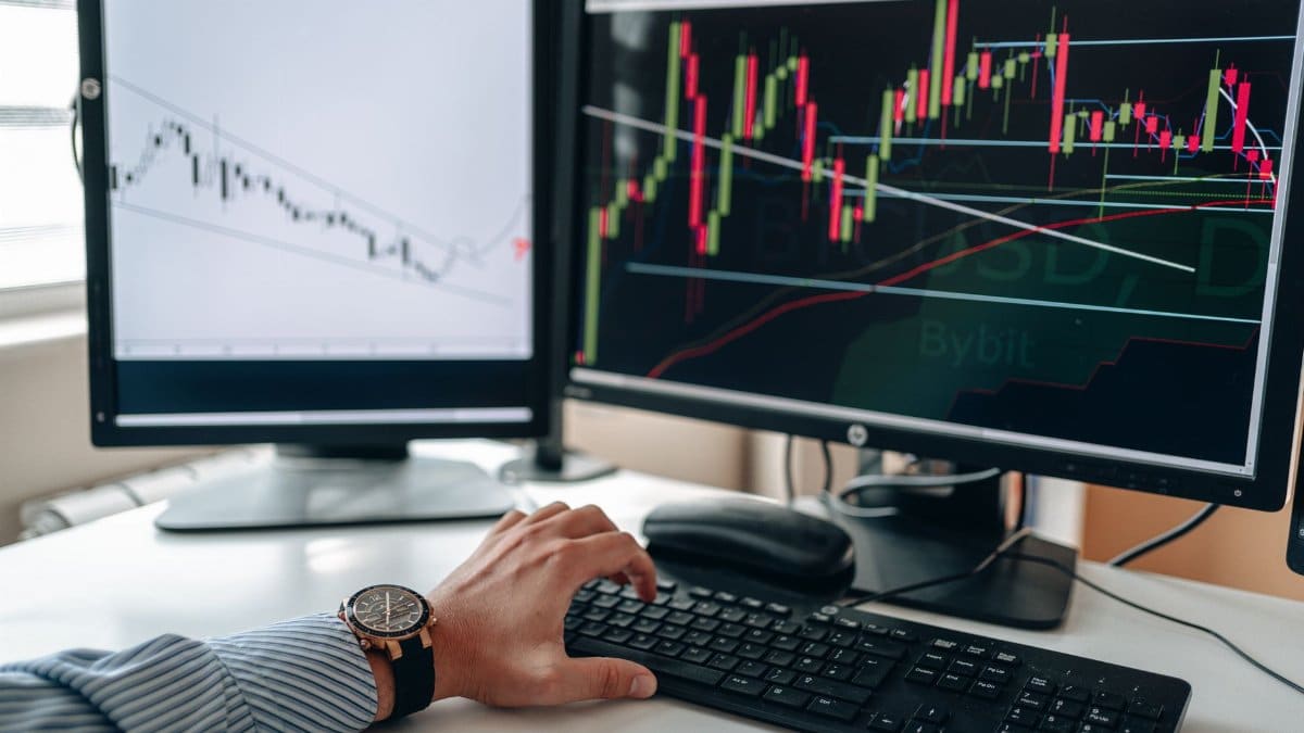A businessperson using dual monitors to analyze stock market trends with charts and graphs.