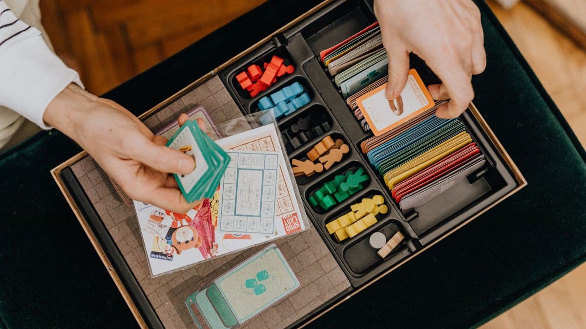 Close-up of hands holding cards in a colorful board game setup, showcasing strategy play.