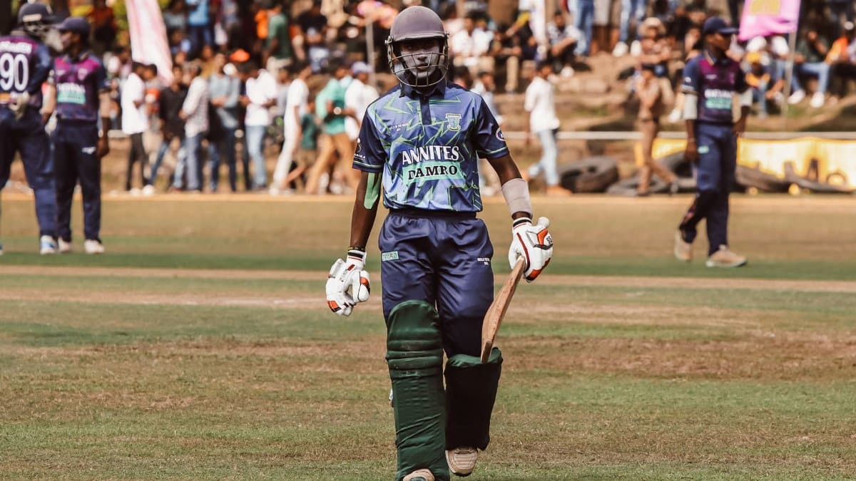 Cricketer wearing protective gear with bat in hand during a match. Crowd and teammates in background.