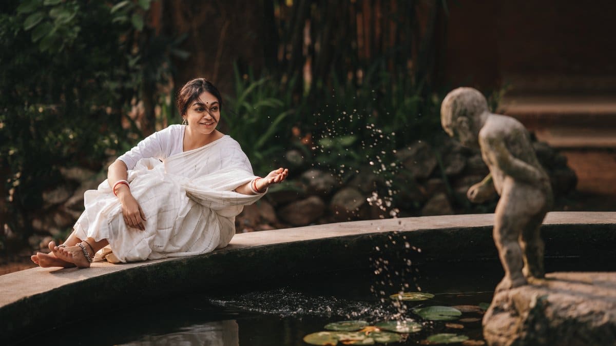 South Asian woman in traditional saree sitting by a pond, enjoying serene moment and nature.