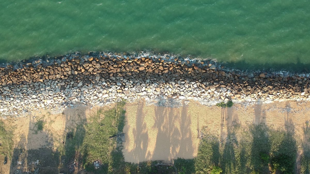 Explore the serene beauty of a rocky shoreline meeting a sandy beach from above.