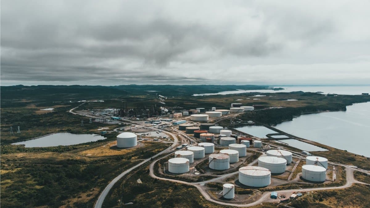 Aerial landscape shot of a coastal oil refinery with storage silos under cloudy skies.