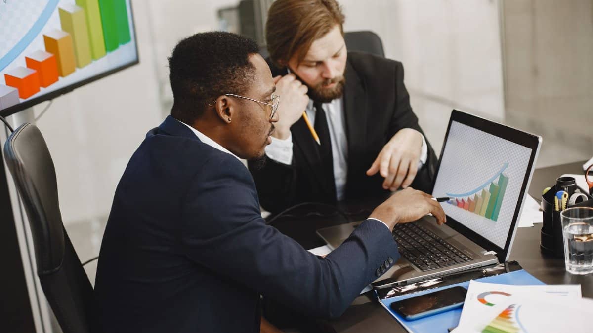 Two business professionals working on growth charts using laptop in an office setting.