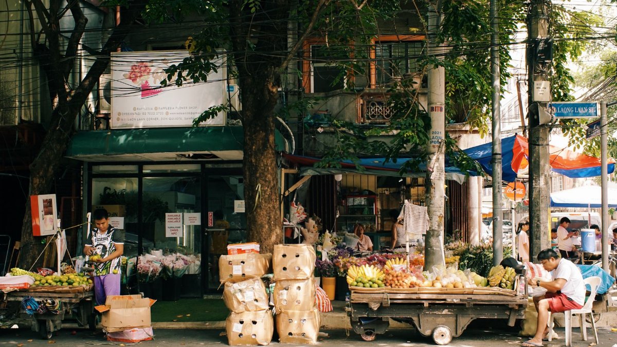 Bustling outdoor market with fruit vendors and street activity in Southeast Asia.