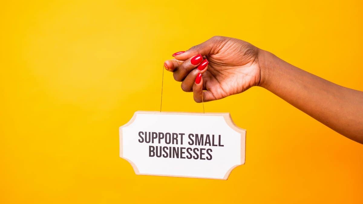 Hand holding a 'Support Small Businesses' sign against a vibrant yellow background, promoting local commerce.