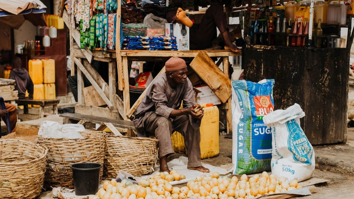 A street vendor in a bustling market selling produce and assorted goods in woven baskets.