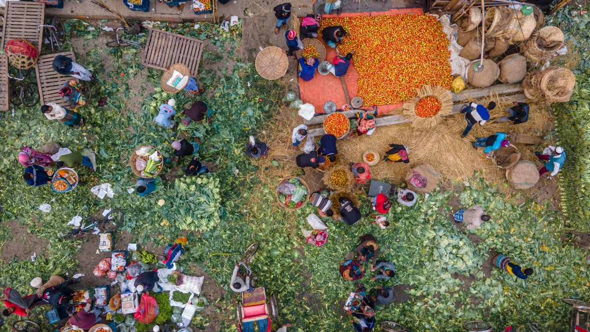 A vibrant aerial scene capturing the bustling activity of an outdoor vegetable market filled with people and vibrant produce.