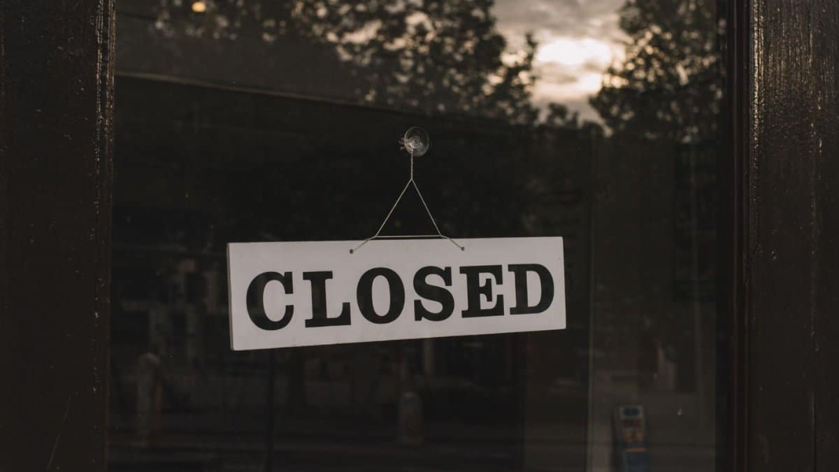 White rectangular sign with word Closed hanging on glass wall of cafe or shop