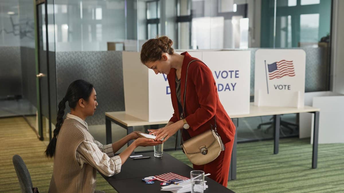 Two women interacting at a registration desk on election day indoors.