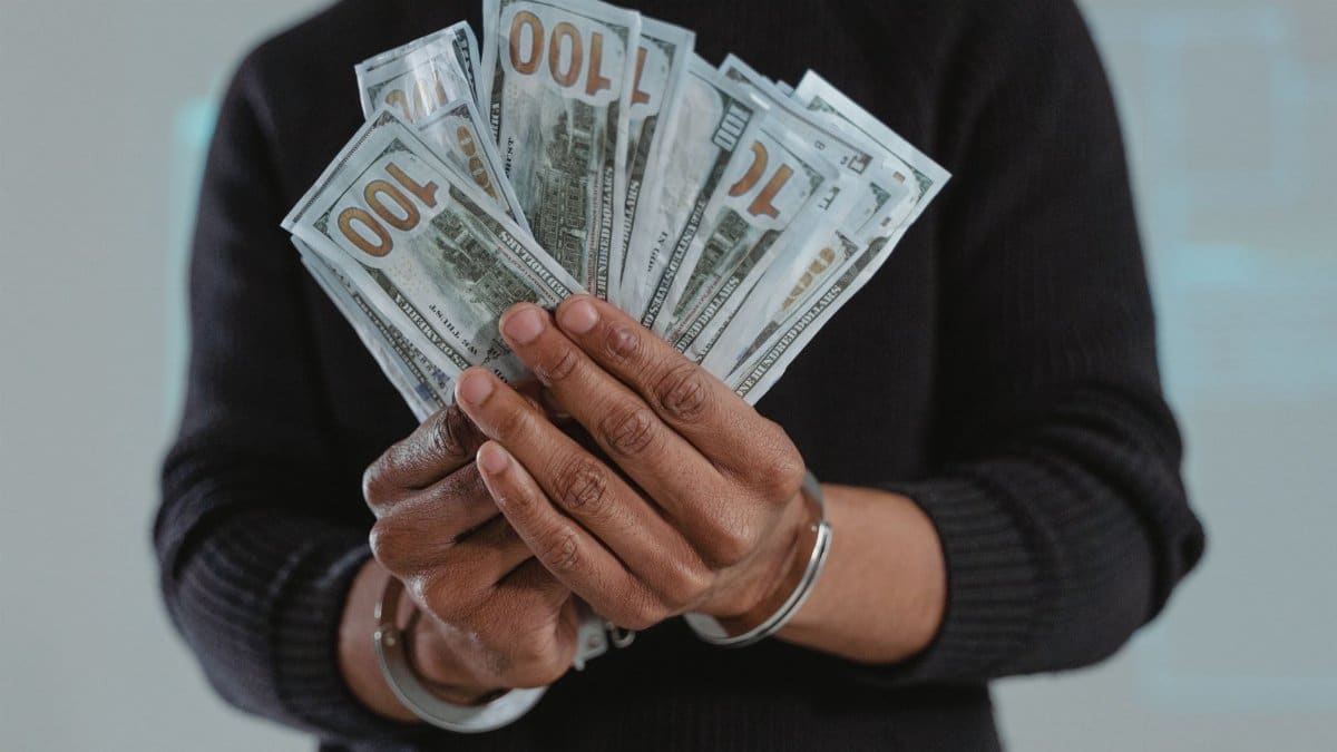 Close-up of hands holding 100-dollar bills while handcuffed, symbolizing crime and punishment.