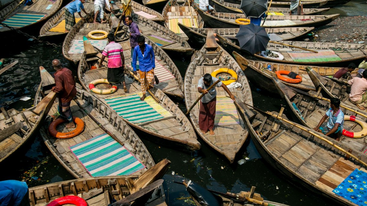 A bustling river market scene with numerous wooden boats and busy vendors on a sunny day.