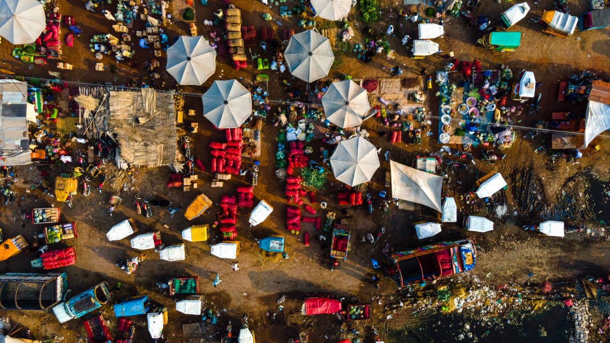 Colorful aerial shot of market stalls with people, umbrellas, and produce.