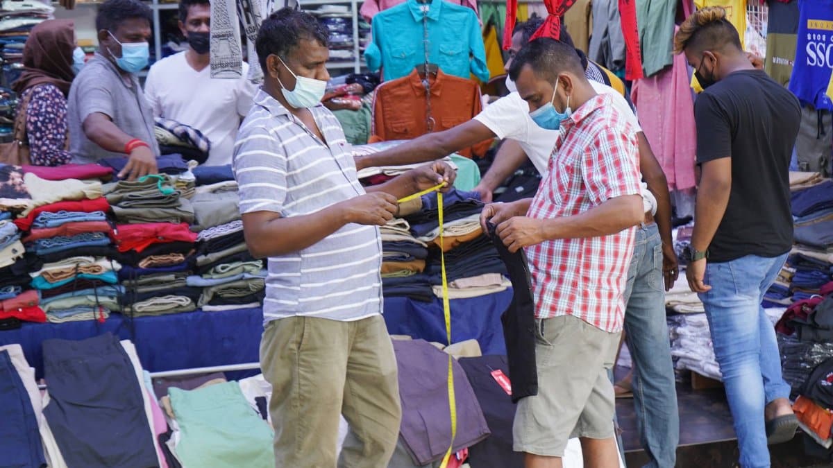 Customers shopping for clothes at a street market, all wearing masks.