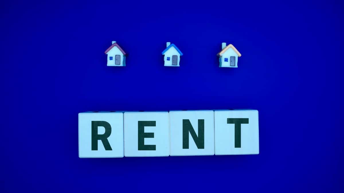 Miniature houses above letters spelling 'RENT' on a blue background, ideal for real estate themes.