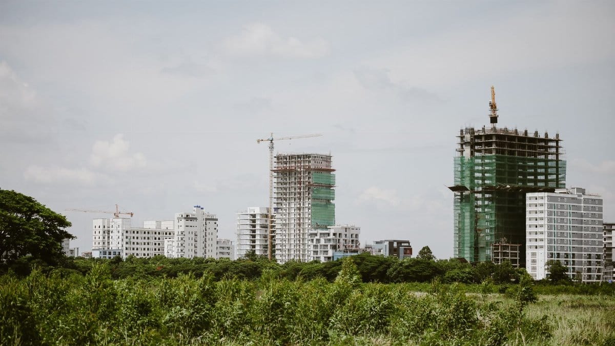 High-rise buildings under construction with cranes in a green landscape.