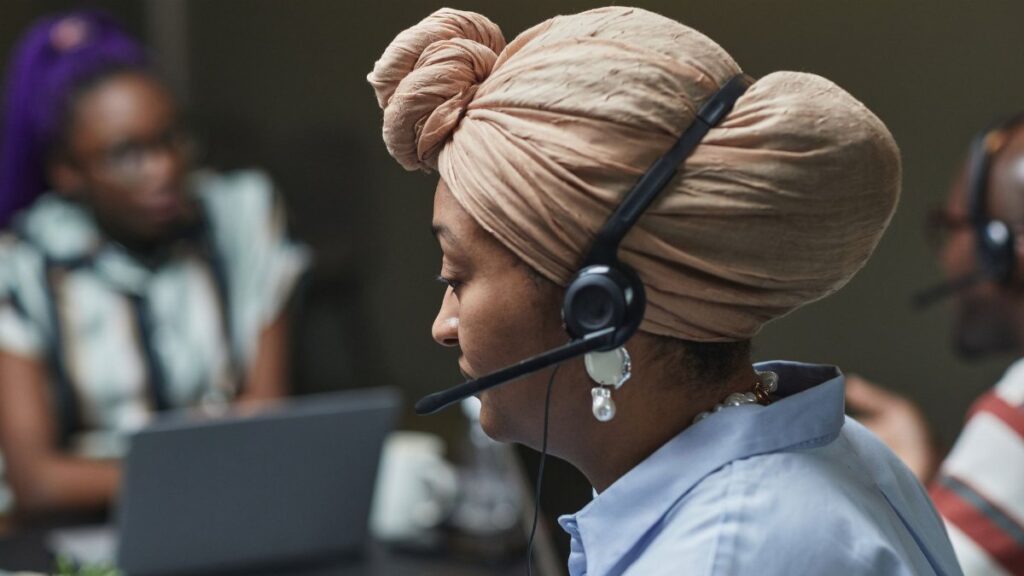 Side profile of a woman in a headscarf working in a call center, wearing a headset and microphone.