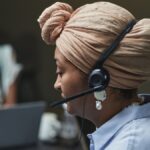Side profile of a woman in a headscarf working in a call center, wearing a headset and microphone.