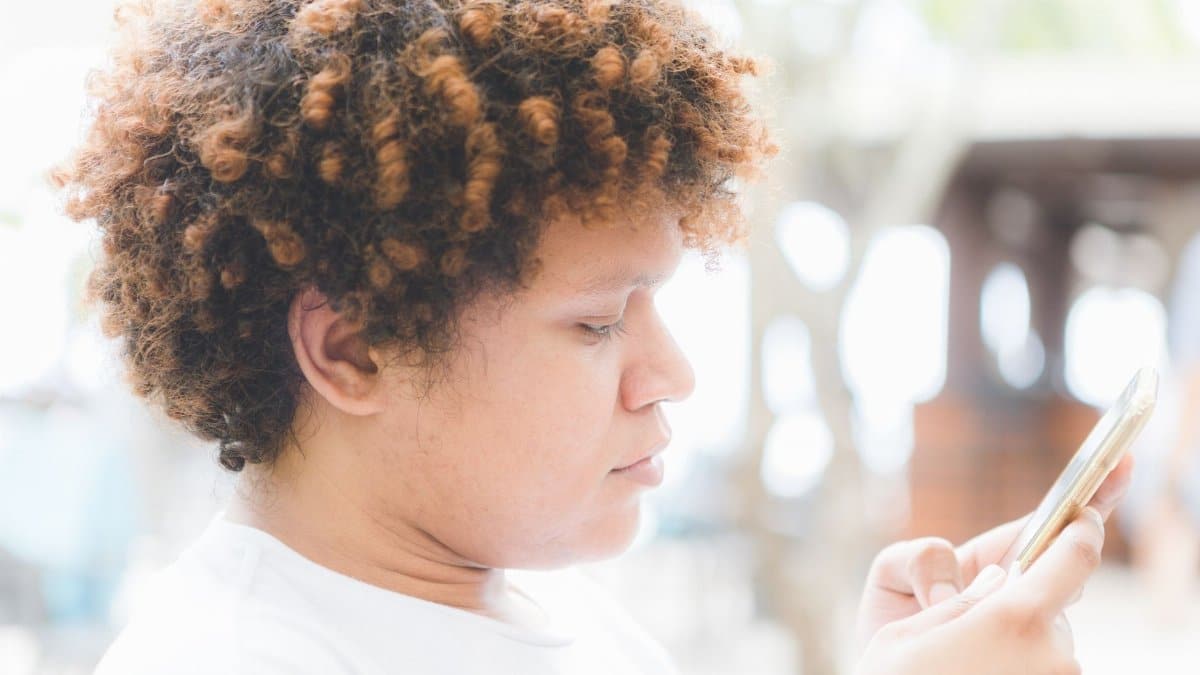 Side view crop concentrated ethnic male with curly hair browsing contemporary mobile phone while spending sunny day on veranda