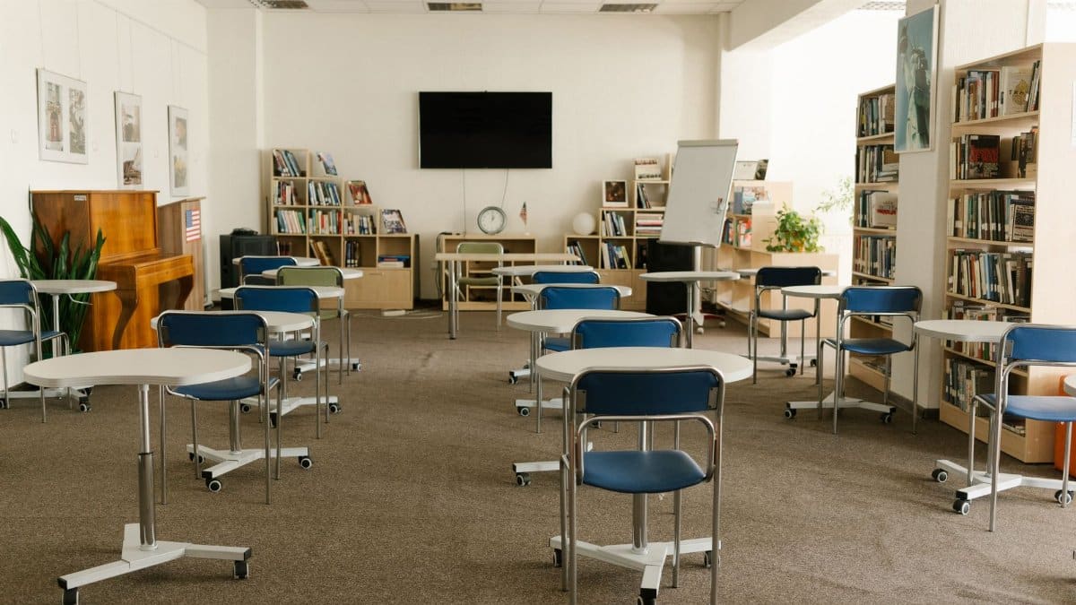 A modern classroom interior featuring bookshelves, chairs, tables, and a television for an educational setting.