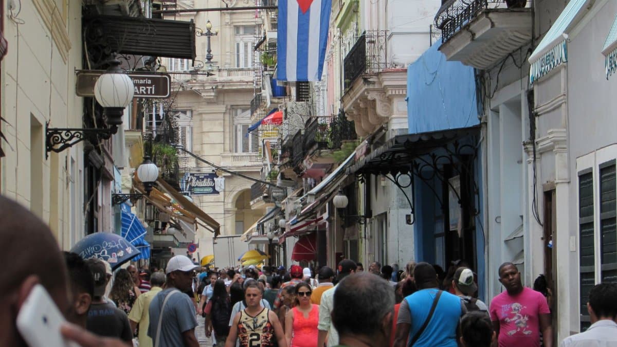 Vibrant street scene on Calle Obispo in Old Havana, Cuba, capturing a lively crowd under the Cuban flag.