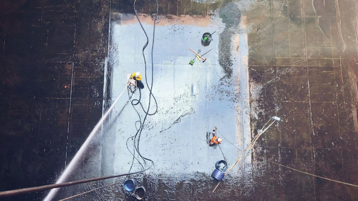 Top view of workers cleaning a large surface with equipment and water hoses.