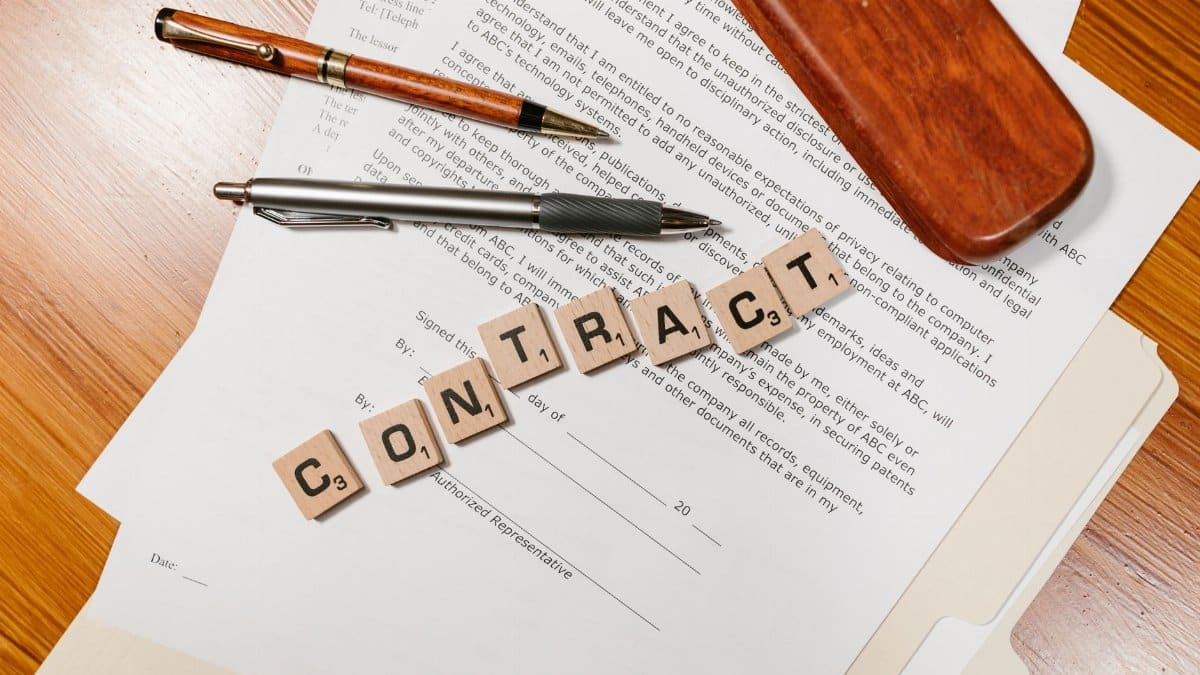 Close-up of contract papers with Scrabble tiles spelling 'CONTRACT'.