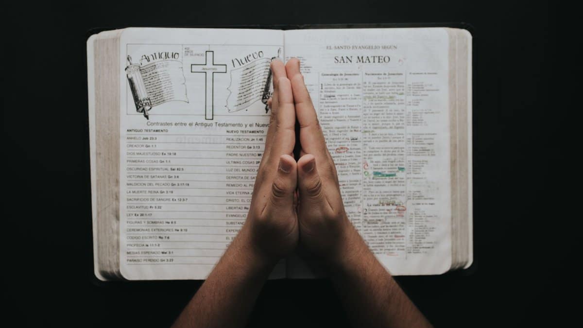 Hands clasped in prayer on an open Bible showing the book of Matthew, emphasizing faith and spirituality.